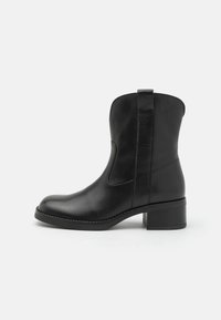 Bota negra de cuero hasta el tobillo con puntera redondeada, paneles laterales elásticos y un tacón bajo cuadrado. Textura suave con detalles de costura mínimos.