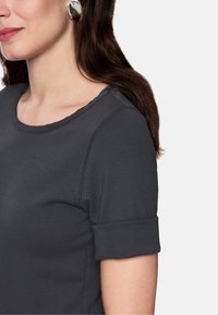 Dunkelgraues Kurzarmoberteil mit rundem Ausschnitt und umgeschlagenen Bündchen. Texturierter Stoff mit sichtbaren Nahtakzenten. Glatte Oberfläche.