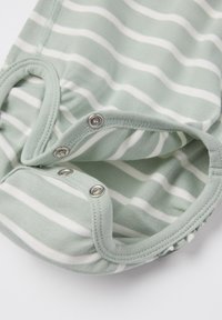 Vihreä mintunvärinen kangas, jossa on valkoisia raitoja, ja alaosassa on nepparit. Pehmeä, puuvilla-tyylinen rakenne, pyöristetyt reunat ja joustava reuna.