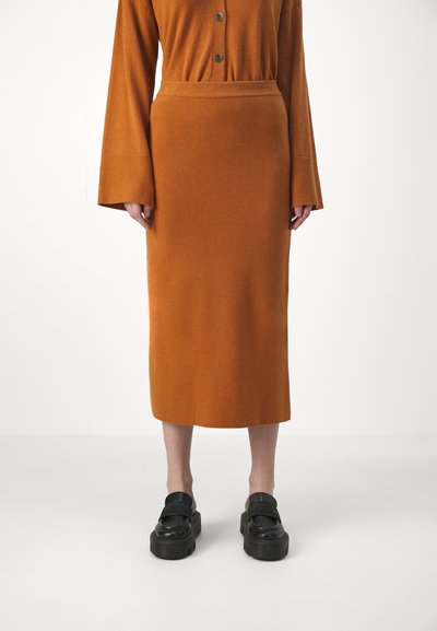 Jupe en tricot orange avec une taille ajustée, s'étendant jusqu'au mollet. Associée à des chaussures à plateforme noires épaisses avec une lanière sur le dessus.