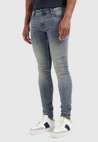 Lichtblauwe skinny jeans met een vervaagde afwerking, met vijf zakken en een mid-rise taille, gecombineerd met witte sneakers met marineblauwe accenten.