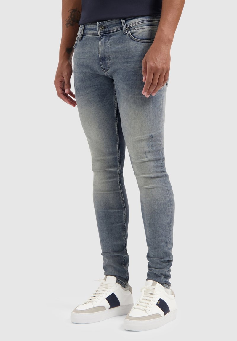 Lichtblauwe skinny jeans met een vervaagde afwerking, met vijf zakken en een mid-rise taille, gecombineerd met witte sneakers met marineblauwe accenten.