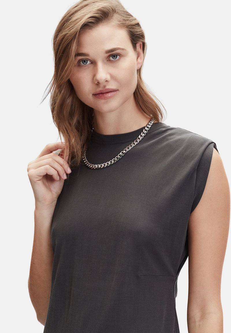 Zwarte mouwloze top met een ronde halslijn en een subtiele textuur. Het model draagt een zilveren ketting, die een ontspannen fit laat zien.