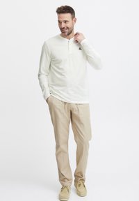 Lys langt ermet henley-skjorte i kremfarge med en knapp-opp hals, kombinert med beige bukser og lyse sko; myk tekstur og avslappet passform.
