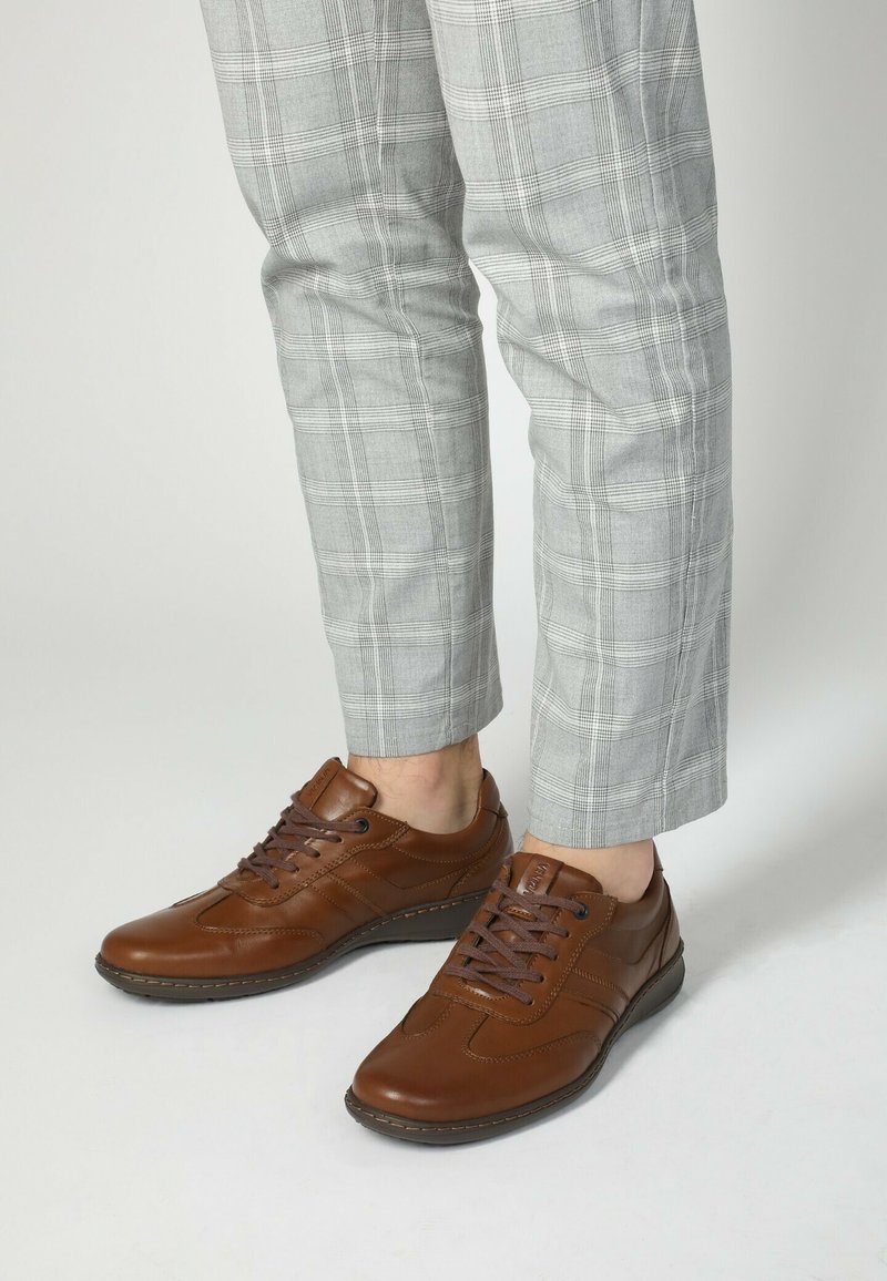 Brązowe skórzane trampki z zaokrąglonym noskiem, płaskimi sznurowadłami i przeszyciami. W zestawie z jasnoszarymi spodniami w kratę.