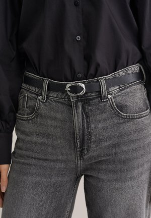 Črn usnjen pas z ovalno srebrno sponko, nošen preko sivih kavbojk z visokim pasom in rahlo zbledelo teksturo ter petimi žepi.