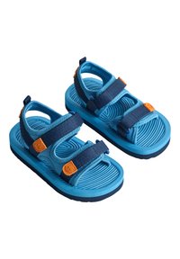 Zilas čības ar teksturētām gumijas zālēm, ar tumši zilām regulējamām siksnām un oranžiem aksesuāriem. Atvērta konstrukcija nodrošina gaisa cirkulāciju un komfortu.