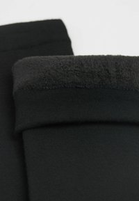 Leggings negros con cintura plegable y un suave forro interior de felpa. Textura suave y diseño ajustado. Sin patrones visibles ni herrajes.