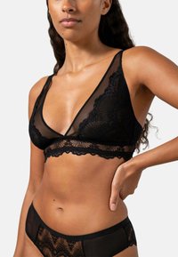 Svart underklädesset bestående av en genomskinlig bh med spetskant och matchande trosor. Bh:n har djup V-ringning och tunna axelband, vilket framhäver intrikata mönster.