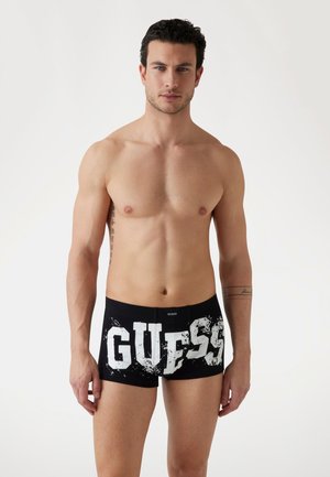 Čierne boxerky s veľkým bielym logom "GUESS" s opotrebovaným efektom, vyrobené z hladkej, elastickej látky.