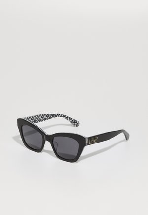Lunettes de soleil noires avec une forme surdimensionnée en œil de chat, lentilles sombres et branches à motif floral noir et blanc. Présente un détail de logo sur le côté.