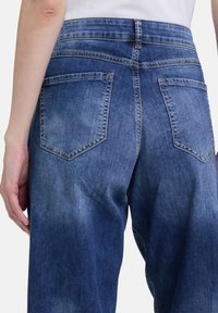 Dunkelblaue Denimjeans mit einer leicht abgetragenen Textur, zwei hinteren Taschen, kontrastierenden Nähten und einer mittelhohen Taille.