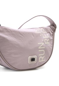 Bolso de hombro de tela de color púrpura claro con forma redondeada, que presenta texto blanco en negrita, costuras decorativas y un pequeño parche de logo negro.
