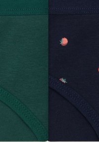 Dwa złożone bawełniane ubrania obok siebie, jedno jednolite ciemnozielone, a drugie granatowe w małe czerwone nadruki pomidorów.