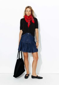 Pull noir à manches courtes, écharpe à motifs rouges, jupe en denim évasée, sac fourre-tout noir et chaussures plates noires avec design découpé.