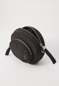Czarna okrągła torba wykonana z nylonu, z dwoma zamykanymi na zamek komorami, wytłoczonym logo oraz materiałowym paskiem. Teksturowana powierzchnia i błyszczące akcesoria.