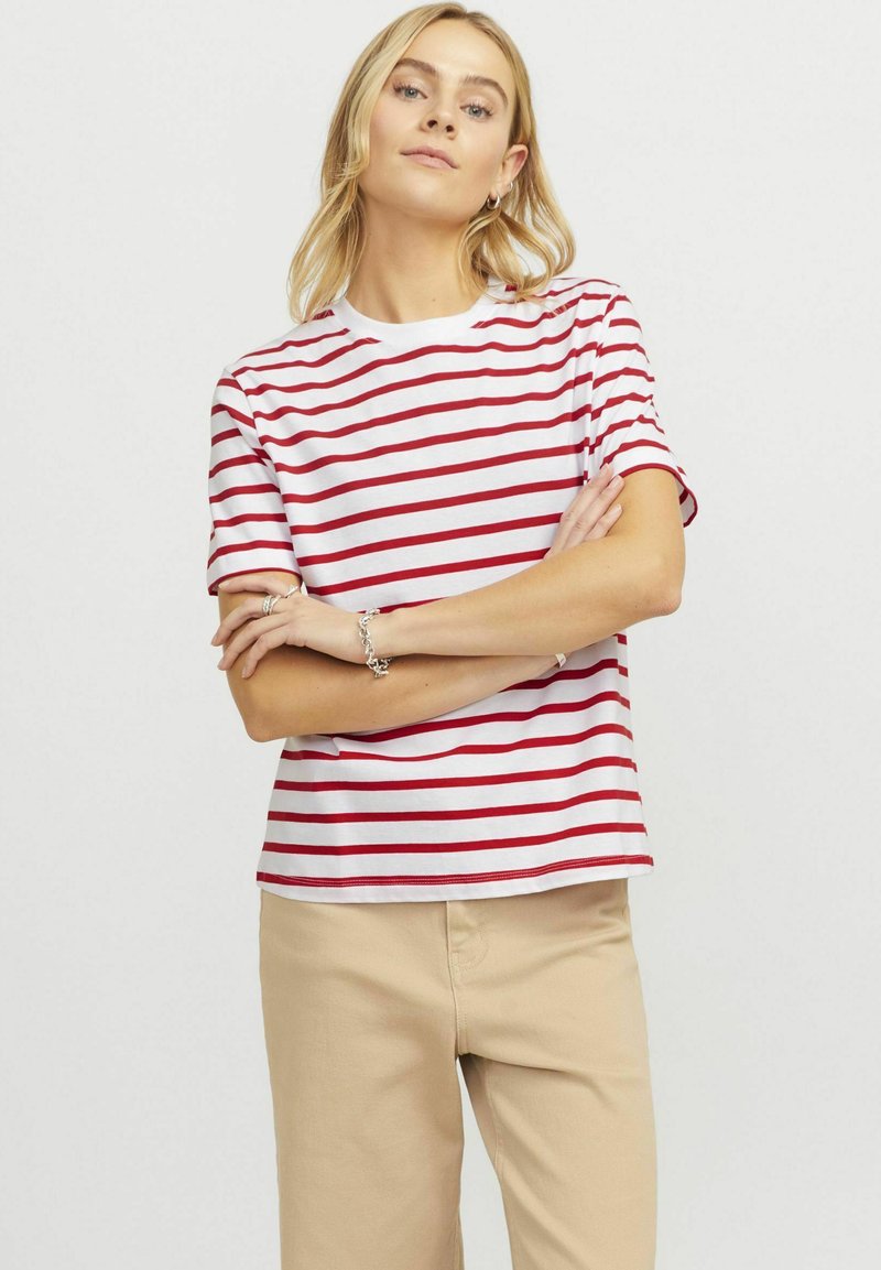T-shirt às riscas vermelha e branca, feita de algodão, apresentando um decote redondo e mangas curtas, combinada com calças bege.