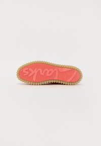 Semelle de chaussure en caoutchouc de couleur pêche avec une texture striée, présentant un motif et un bord arrondi. Accentuée d'un contour de couleur crème.