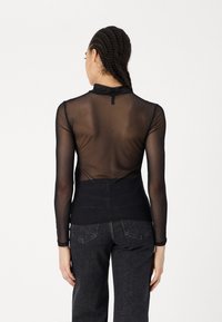 Svart langermet topp laget av gjennomsiktig materiale; har høy krage og lukking bak. Kombinert med mørke, høyt liv jeans.