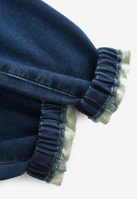 Denimriietusega, millel on volangkäised. Tumedast sinisest kangast, millel on sile tekstuur ja helesinised aktsendid volangservadel.