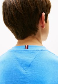 T-shirt di cotone azzurro chiaro a maniche corte, con dettagli a righe orizzontali in rosso, bianco e blu sul colletto e una cucitura strutturata.