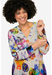 Meerkleurige tuniek met een v-hals, voorzien van abstracte patronen, vredestekens en hartmotieven. Lange mouwen met zwarte manchetten.