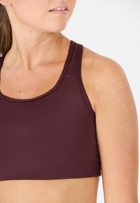 Maroon sportbh med rundad halsringning, breda axelband och slät, elastisk tyg. Har platta sömmar för komfort och en åtsittande design.