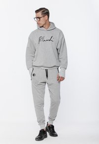 Szara bluza z kapturem z charakterystycznym nadrukiem, w zestawie z pasującymi dresami. Posiada elastyczny pas i mankiety, dopełnione czarnymi sneakersami.