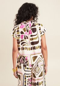 Blusa a stampa floreale con maniche corte, caratterizzata da motivi rosa, verdi e marroni su uno sfondo crema; dettaglio al collo con lacci sul retro.