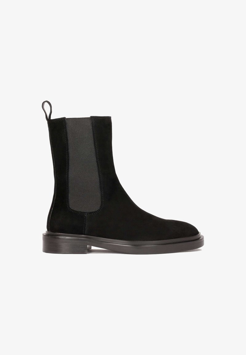 Bottine Chelsea en daim noir avec panneau latéral élastique, languette à l’arrière et petit talon empilé sur fond blanc.
