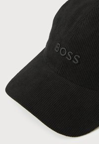 Svart kordfløyelslue med en brodert "BOSS"-logo i matchende farge på frontpanelet, med en strukturert skjerm.