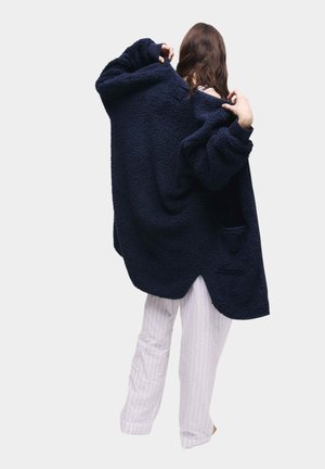 Marineblauwe fleece oversized jas met een gestructureerd oppervlak, drop schouders en zijzakken, gecombineerd met witte gestreepte pyjamabroek.
