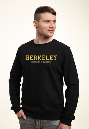 Felpa nera con maniche lunghe e scollo tondo, caratterizzata da un audace testo giallo: "UNIVERSITÀ DI BERKELEY CALIFORNIA." Texture morbida.