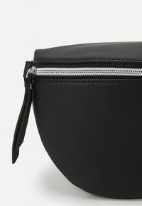 Zwartleren pouch met een gestructureerde afwerking, voorzien van een zilveren rits en trekband aan de zijkant. Ronde vorm met witte stikseldetails.