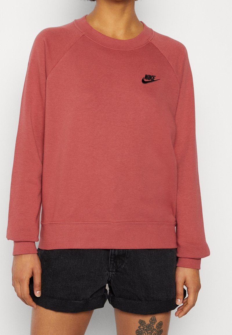 Mikina Nike v dusty rose, s raglánovými rukávy a žebrovanými manžetami. Černé logo na hrudi. Materiál vypadá měkký a hladký na dotek.