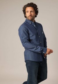 Marineblauwe blouse met knopen en een borstzak, gemaakt van katoen, met een subtiele textuur en lange mouwen, gecombineerd met donkere jeans.