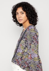 Blusa floral com fundo azul marinho escuro, várias flores coloridas, design em forma de V e mangas longas com detalhes franzidos.
