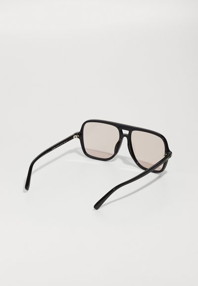 Gafas de sol negras con montura cuadrada, lentes ahumados de color marrón claro y patillas negras elegantes. Presenta un diseño sencillo y moderno, sin adornos.