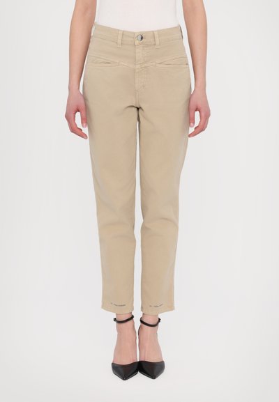 Pantalones recortados beige con una textura suave, que presentan bolsillos, un cierre de botón y detalles de costura en contraste. Combinados con tacones negros.