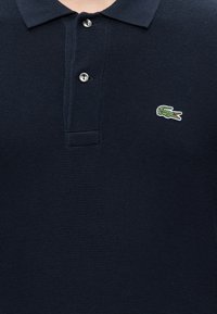 Polo bleu marine avec deux boutons et un petit logo crocodile vert brodé sur la poitrine gauche.