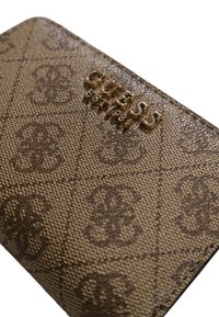 Portefeuille marron à motifs en tissu texturé, avec une finition brillante et le nom de la marque "GUESS" embossé en doré.