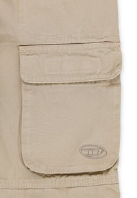 Taschina in tessuto beige con chiusura a patella, caratterizzata da una contorno cucito e un accento di logo circolare. Texture liscia e design pratico.