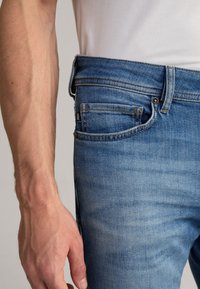 Jeans in denim leggeri blu con una vestibilità slim, caratterizzati da un leggero effetto invecchiato, cuciture a contrasto e una piccola etichetta sulla tasca posteriore.