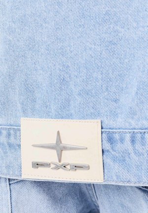 Tessuto di denim azzurro chiaro con una toppa in pelle che presenta un logo a stella in argento metallizzato e le lettere "PXP." Dettagli visibili di cuciture e texture.