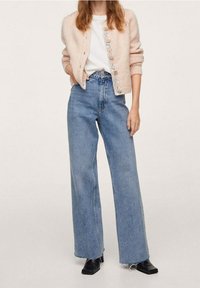 Jasnoróżowy sweter kardigan z kwiatowymi guzikami, biała koszulka i wysokie, szerokie spodnie dżinsowe. Całość uzupełniają czarne botki za kostkę.