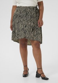 Knielanger, wickelähnlicher Rock im beige-grünen Zebra-Muster, aus leichtem Stoff. Mit einem seitlichen Bindeband und einem asymmetrischen Saum.