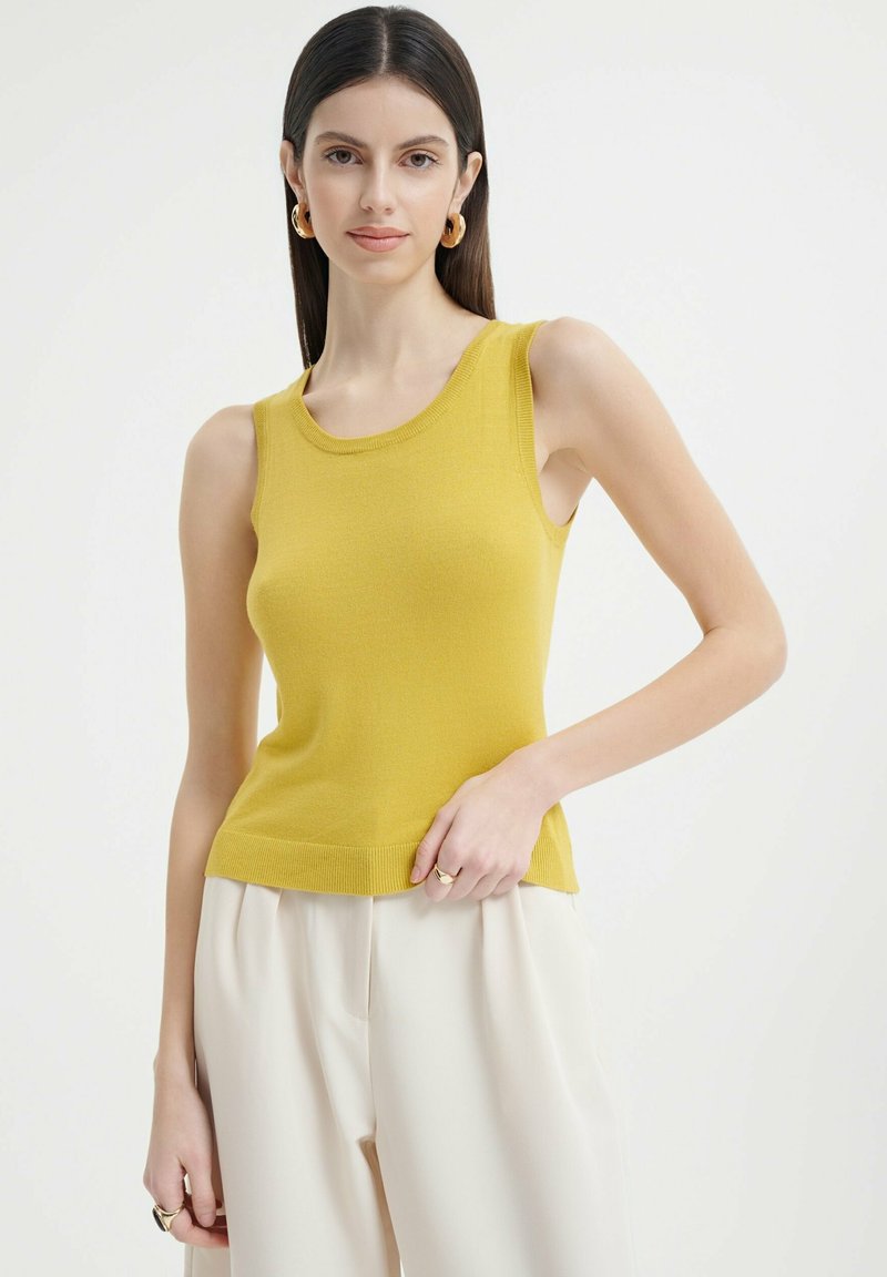 Top sin mangas amarillo con escote redondo y textura acanalada, combinado con pantalones anchos de color claro. Diseño simple, estilo casual.