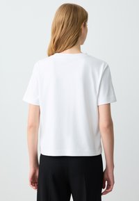 Witte t-shirt met korte mouwen en ronde hals, zachte textuur, relaxte pasvorm en rechte zoom, gecombineerd met zwarte broek.