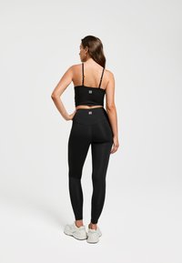 Zwarte sport-bh en high-waisted leggings gemaakt van rekbaar materiaal, met logodetails. Afgewerkt met witte sportschoenen.