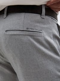 Calças cinzas texturizadas com um padrão subtil, apresentando um bolso nas costas, um logo e um cinto preto na cintura.